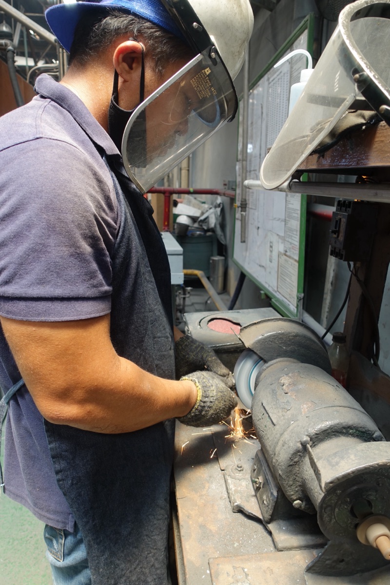 A Metercor worker in a face shield grinding a casting at the bench