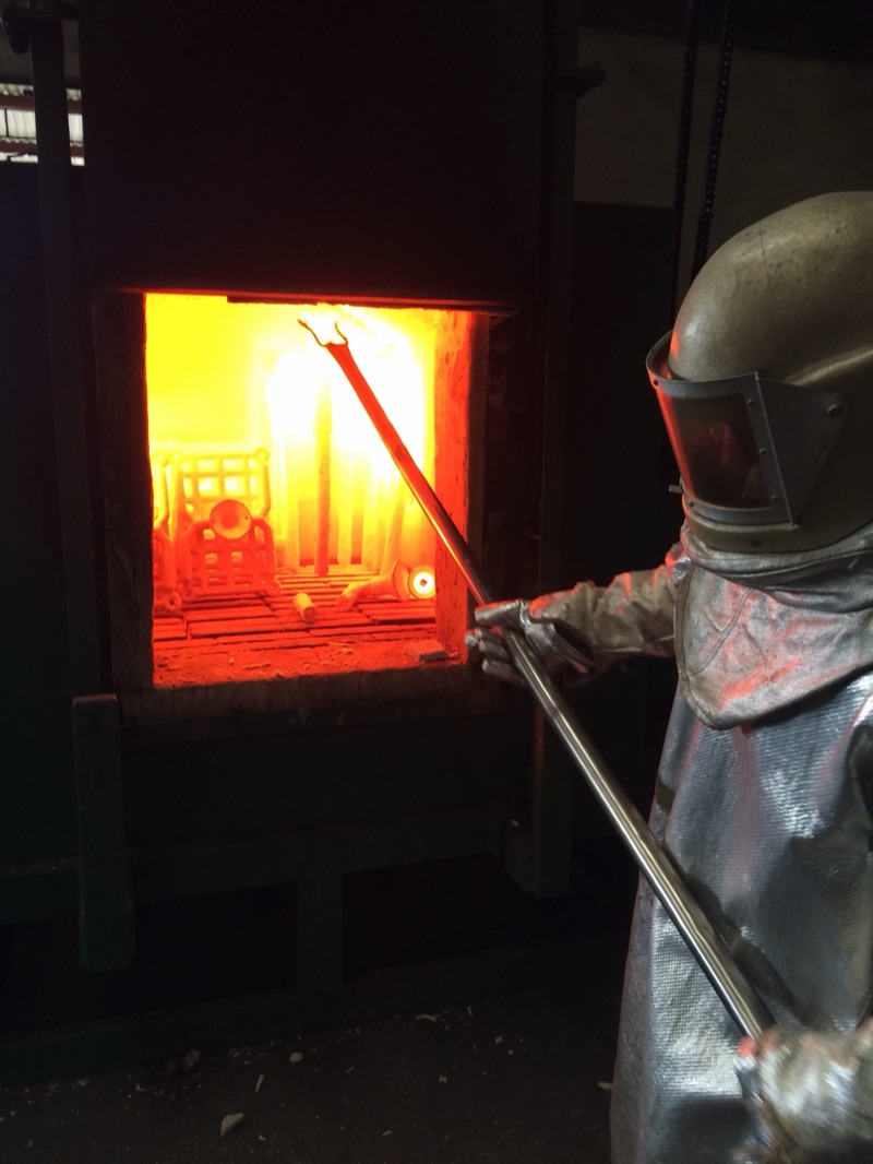 Operator in an aluminized suit draws a glowing ceramic shell mold from the investment casting furnace